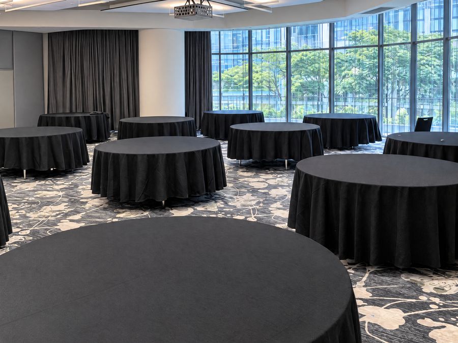 Function room of dressed round tables in front of floor to ceiling windows and greenery