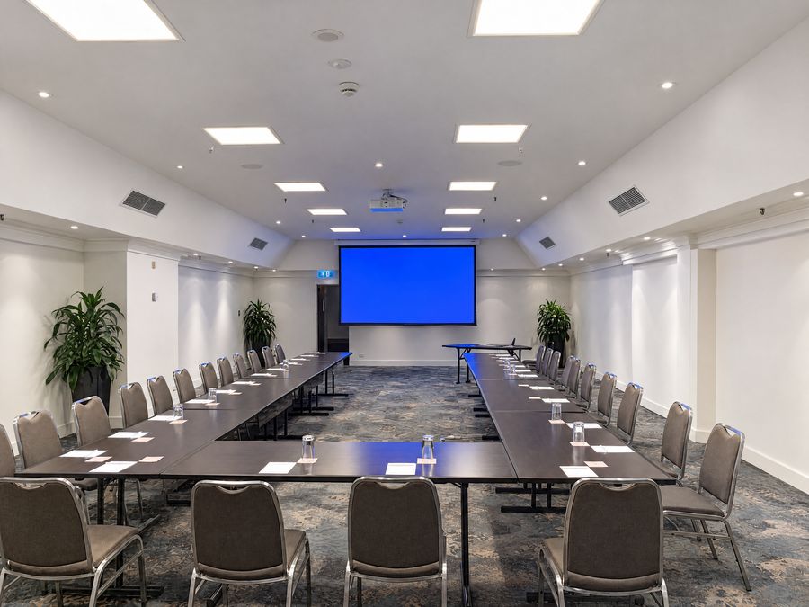 Meeting room set in a U-shape facing a projection screen, water glasses and notepads at every place