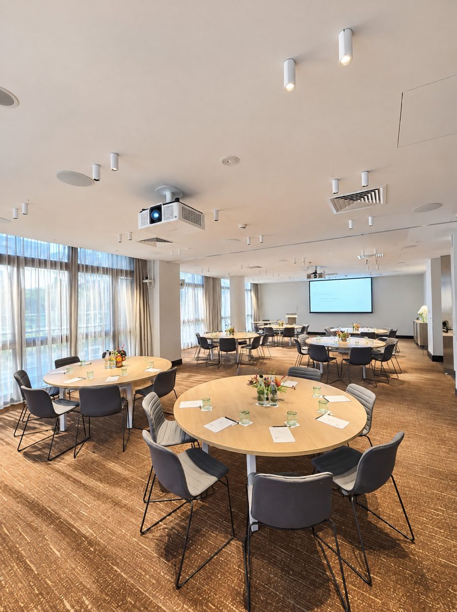 Adina Sydney Darling Harbour, meeting room set with round tables, a screen at the far end and floor to ceiling windows