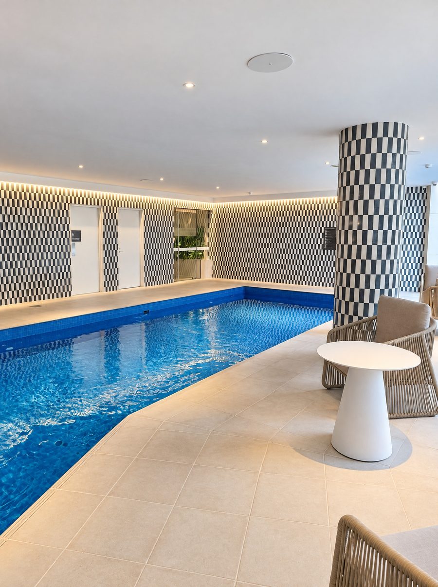 Adina Sydney Darling Harbour, pool with blue mosaic tiles, checked tile walls and a round side table on the pale stone deck
