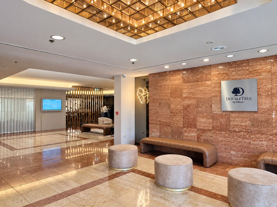 DoubleTree by Hilton Esplanade Darwin, lobby with a polished stone floor, round ottomans and a leather bench below a gold lattice ceiling light