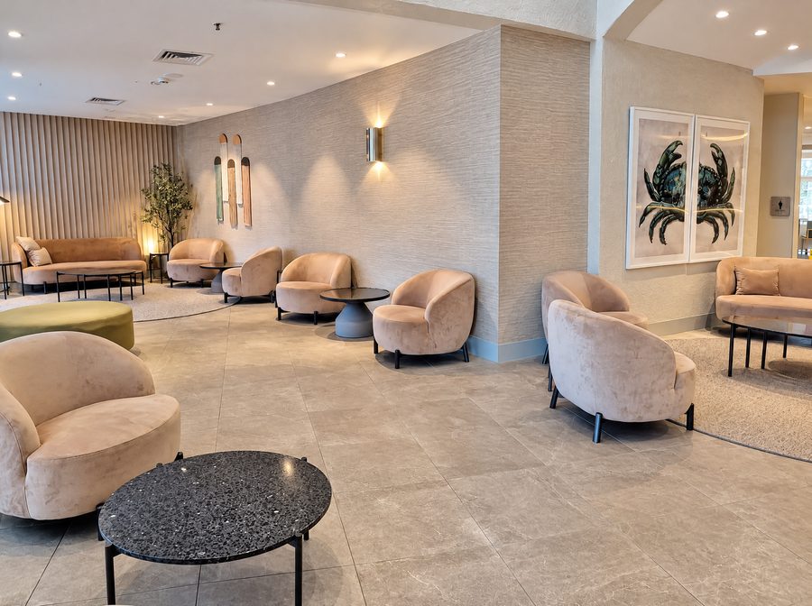 DoubleTree by Hilton Esplanade Darwin, lounge of velvet tub chairs and stone coffee tables along a textured wall, a framed crab print on the right