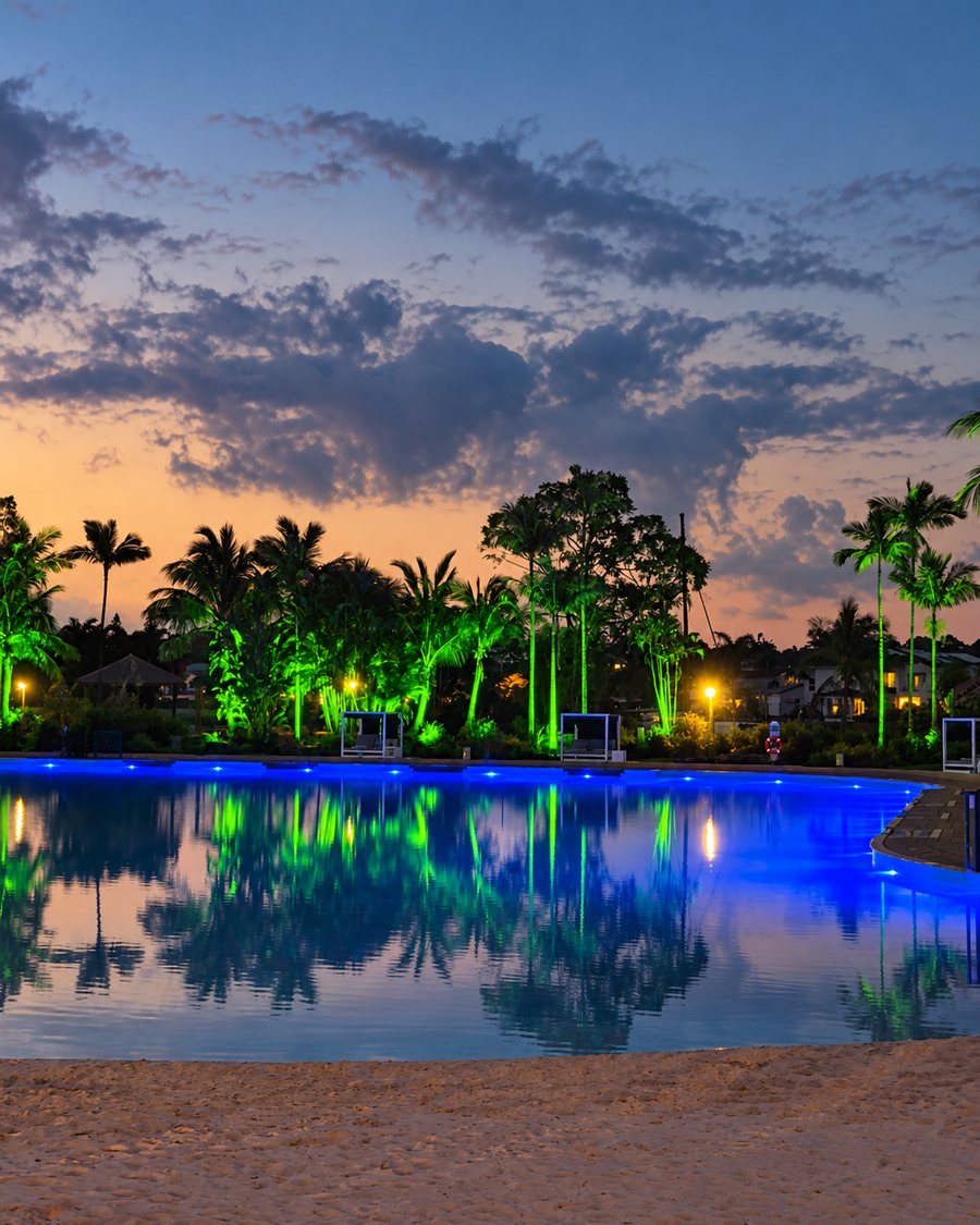 InterContinental Sanctuary Cove Resort, lagoon pool and sand beach at dusk, with the palms lit green