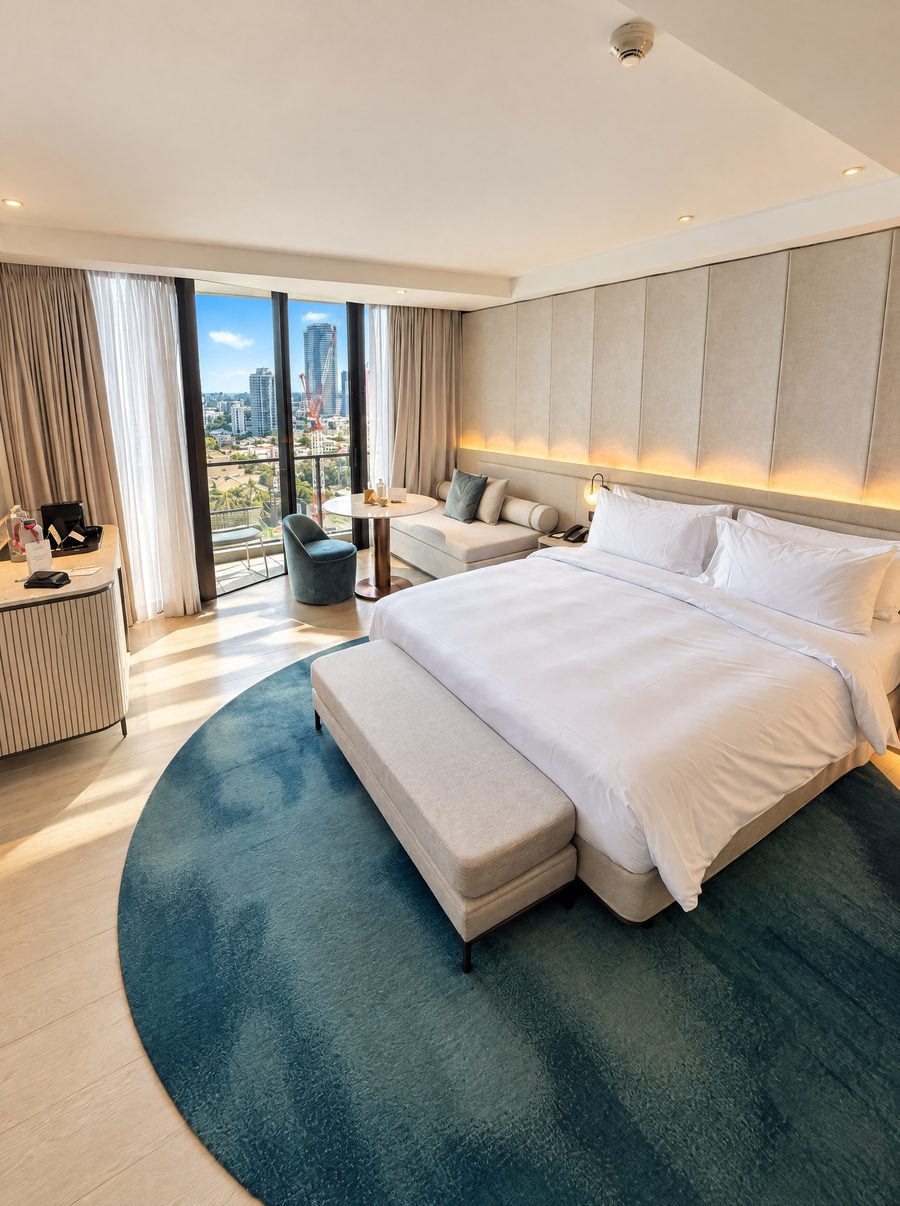 JW Marriott Gold Coast Resort & Spa, guest room with a king bed against a padded headboard wall, a round teal rug and floor to ceiling windows to a balcony