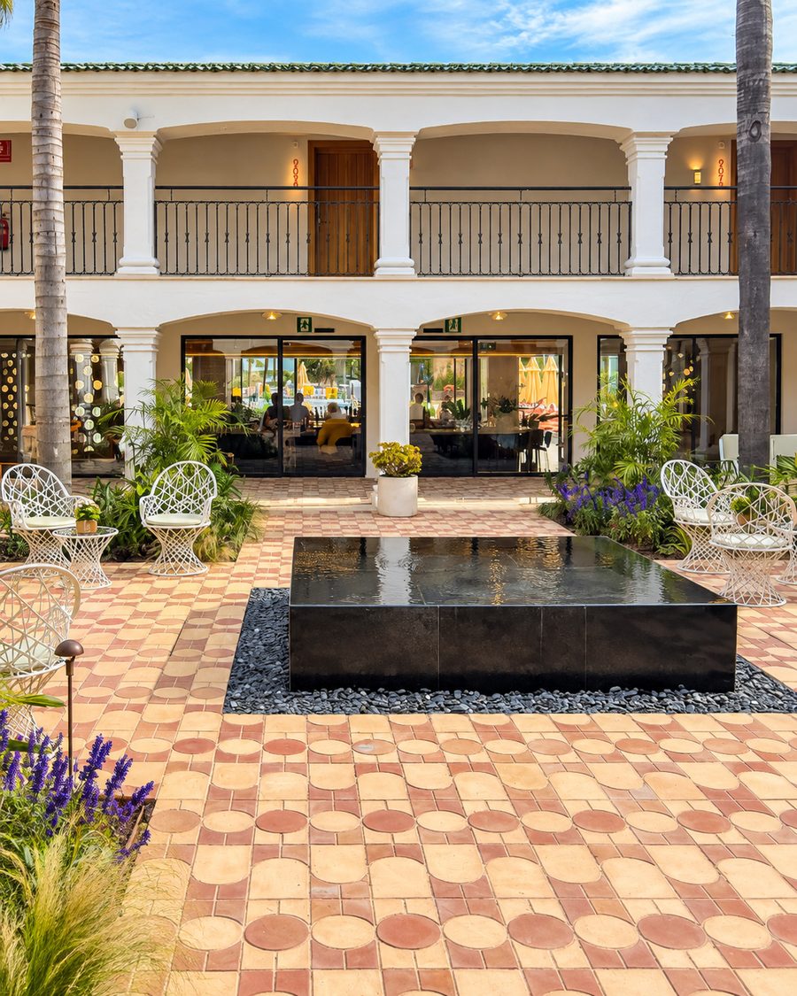 Kimpton Los Monteros Marbella, courtyard with a black water feature, patterned terracotta paving and white wire chairs