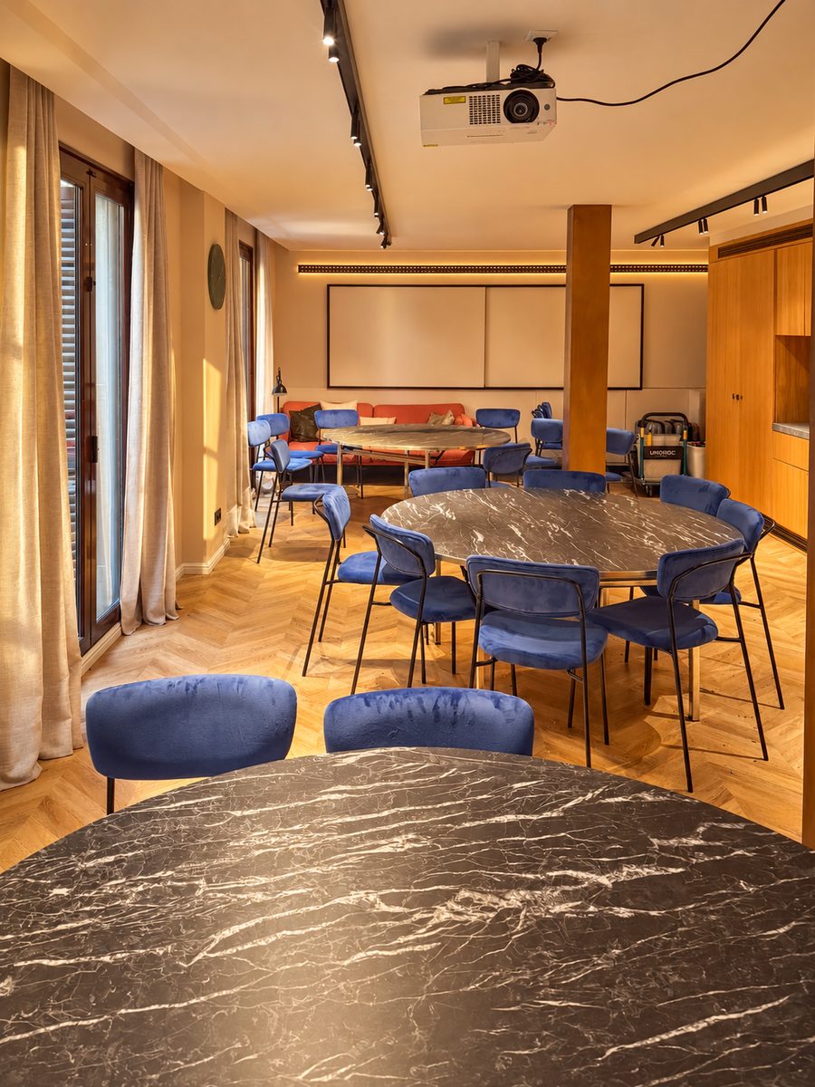 Kimpton Vividora Barcelona, meeting room with round marble topped tables, blue velvet chairs, a projector and a screen