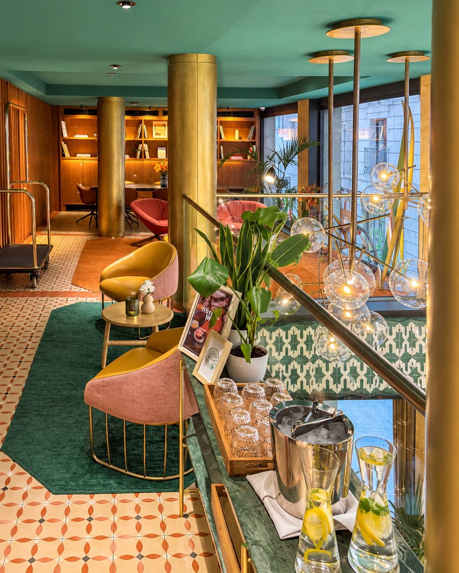 Kimpton Vividora Barcelona, mezzanine lounge with brass columns, mustard chairs, a green rug and a water station