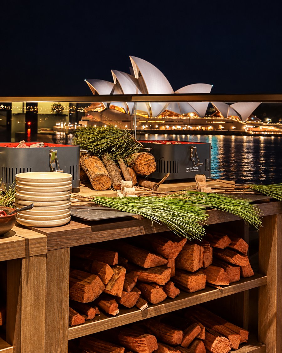 Park Hyatt Sydney, charcoal grills and a stacked timber station on a terrace at night, the Opera House lit across the water