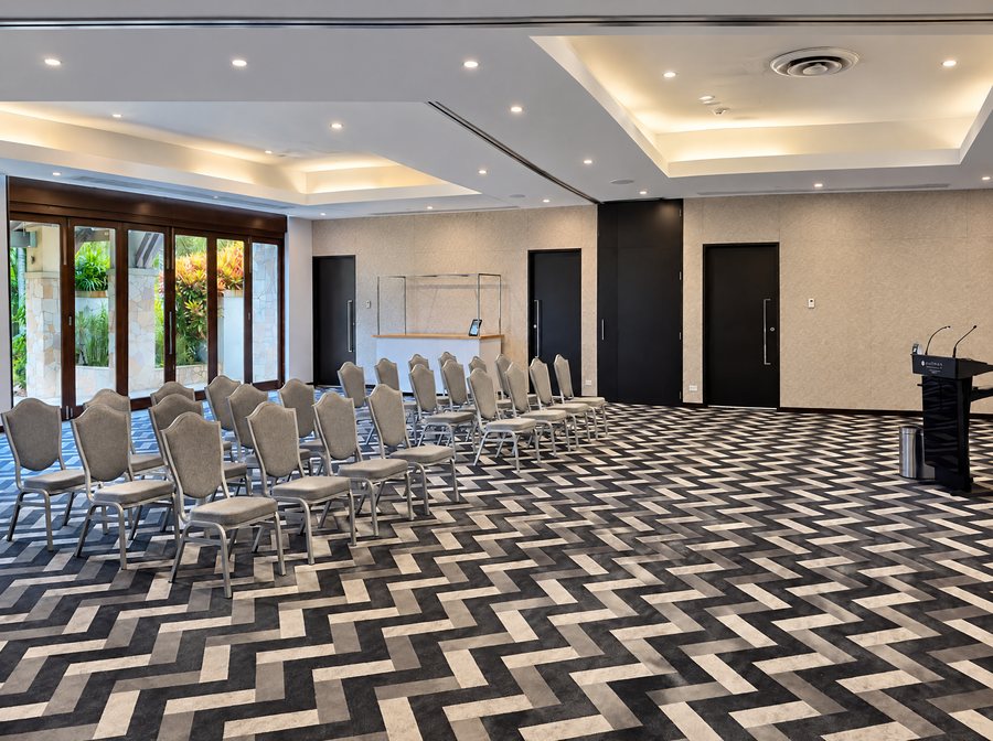 Pullman Port Douglas Sea Temple Resort & Spa, function room set with rows of grey chairs on a black and white herringbone carpet, bifold doors open to a garden on the left and a lectern on the right
