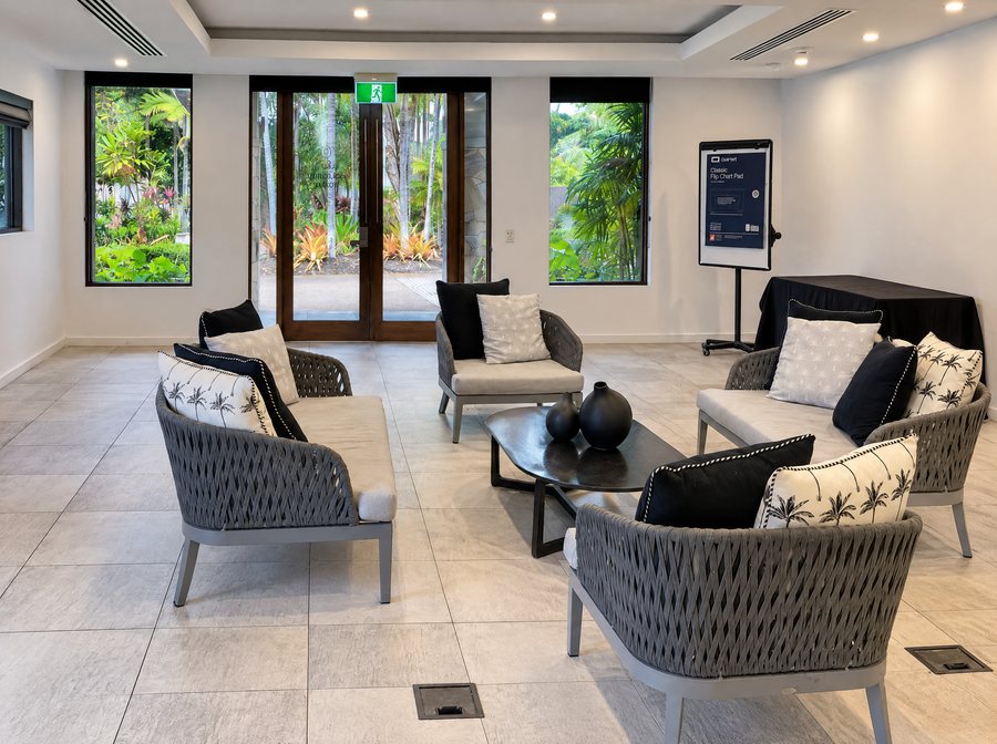 Pullman Port Douglas Sea Temple Resort & Spa, room set as a lounge, woven rope sofas with palm print cushions around a black oval table, glass doors and windows onto tropical garden
