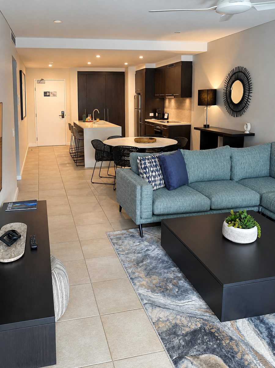 Pullman Port Douglas Sea Temple Resort & Spa, apartment living room with a green corner sofa and a black square coffee table on a marbled rug, the kitchen island and dining table behind
