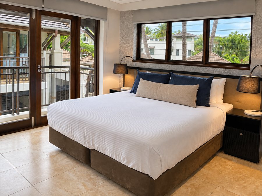 Pullman Port Douglas Sea Temple Resort & Spa, king bed between two black lamps under a wide window, glass doors to a balcony on the left