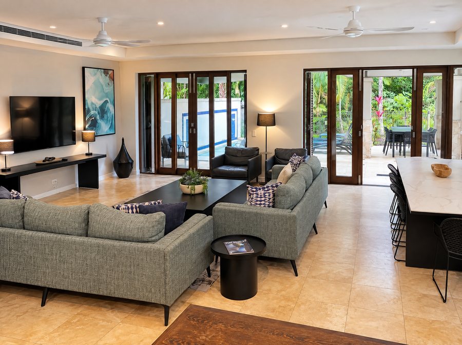 Pullman Port Douglas Sea Temple Resort & Spa, open plan living room, two green sofas and two leather armchairs around a black coffee table, bifold doors open to a covered terrace and plunge pool