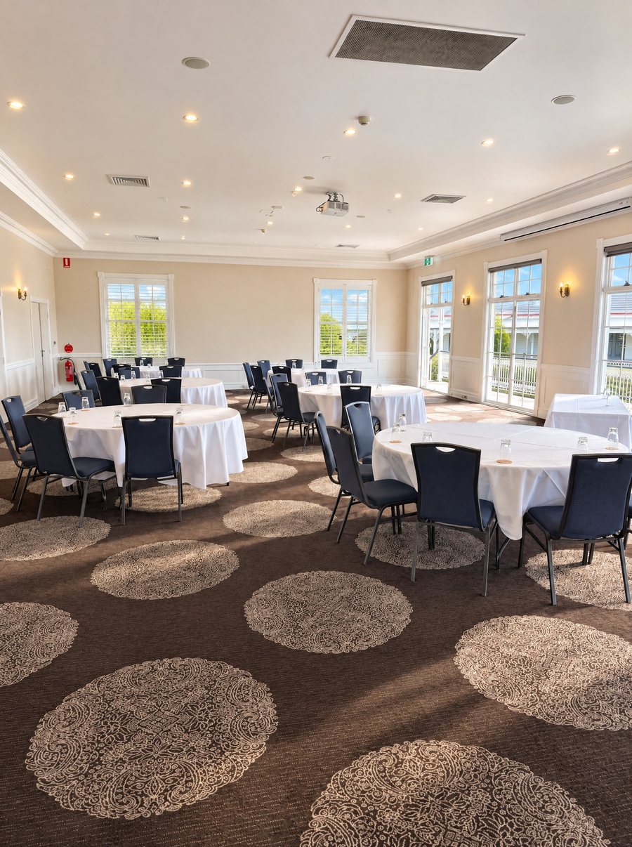 voco Kirkton Park Hunter Valley, function room set with round tables in white linen and navy chairs on a patterned carpet, shuttered windows and French doors along two walls, daylight across the floor
