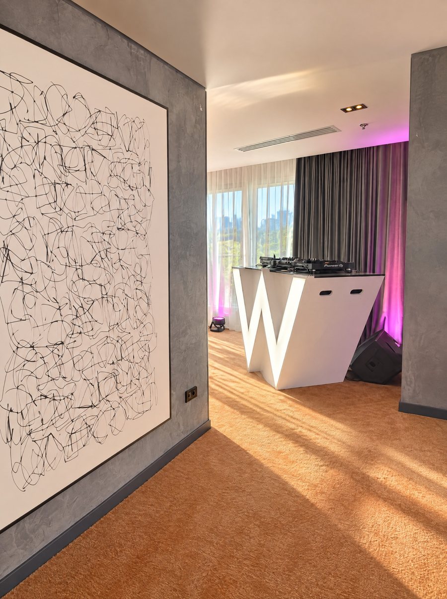 W Sydney, white W shaped DJ booth under pink uplighting in front of full length curtains, a large black line artwork on a grey wall in the foreground